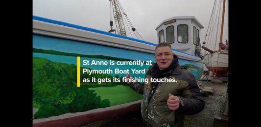 an artist in front of a boat with a painted mural